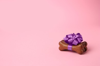 Bone shaped dog cookies with purple bow on pink background, space for text