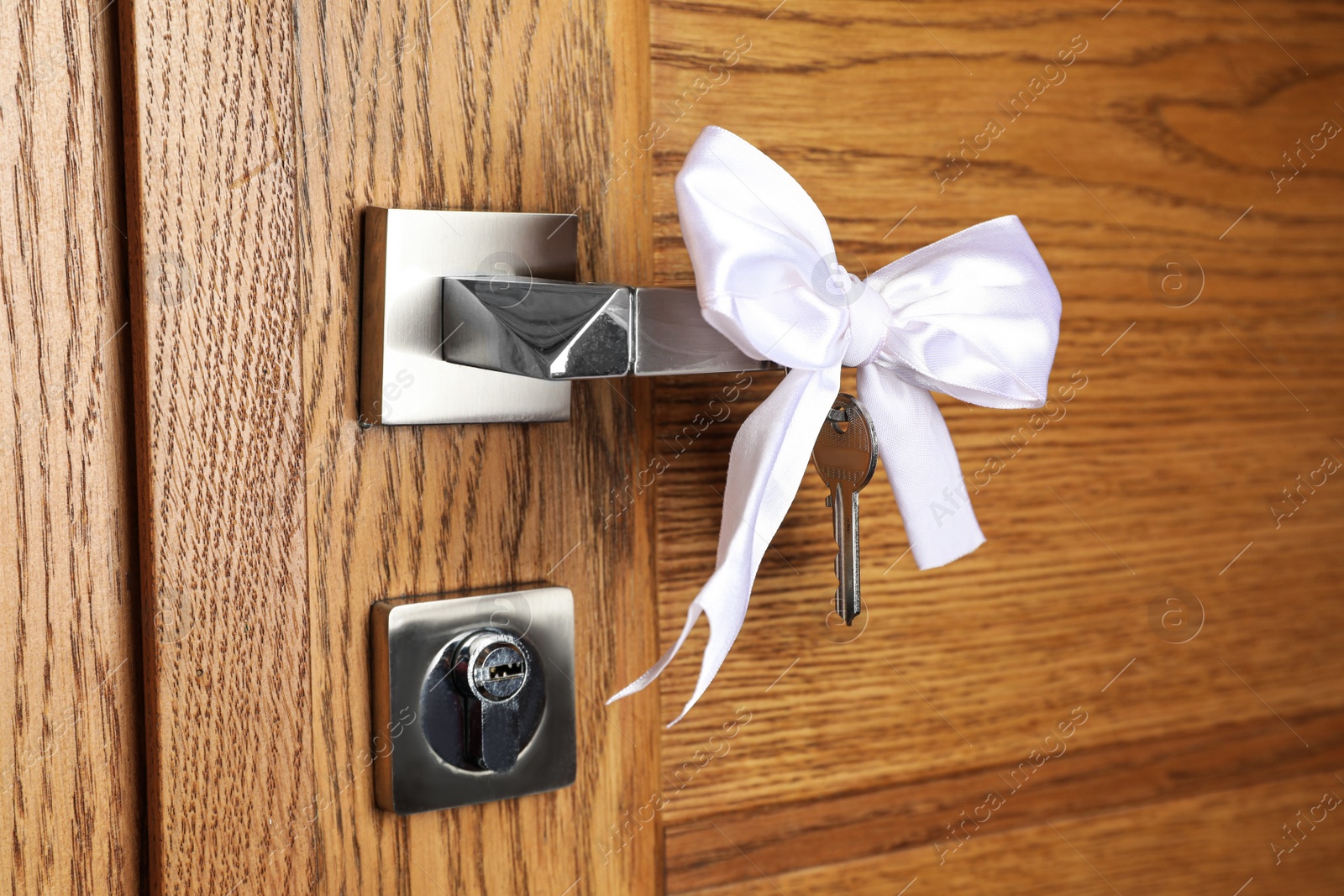 Photo of Key with white bow on door handle, closeup view. Housewarming party