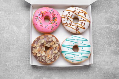 Box with different tasty glazed donuts on light grey table, top view