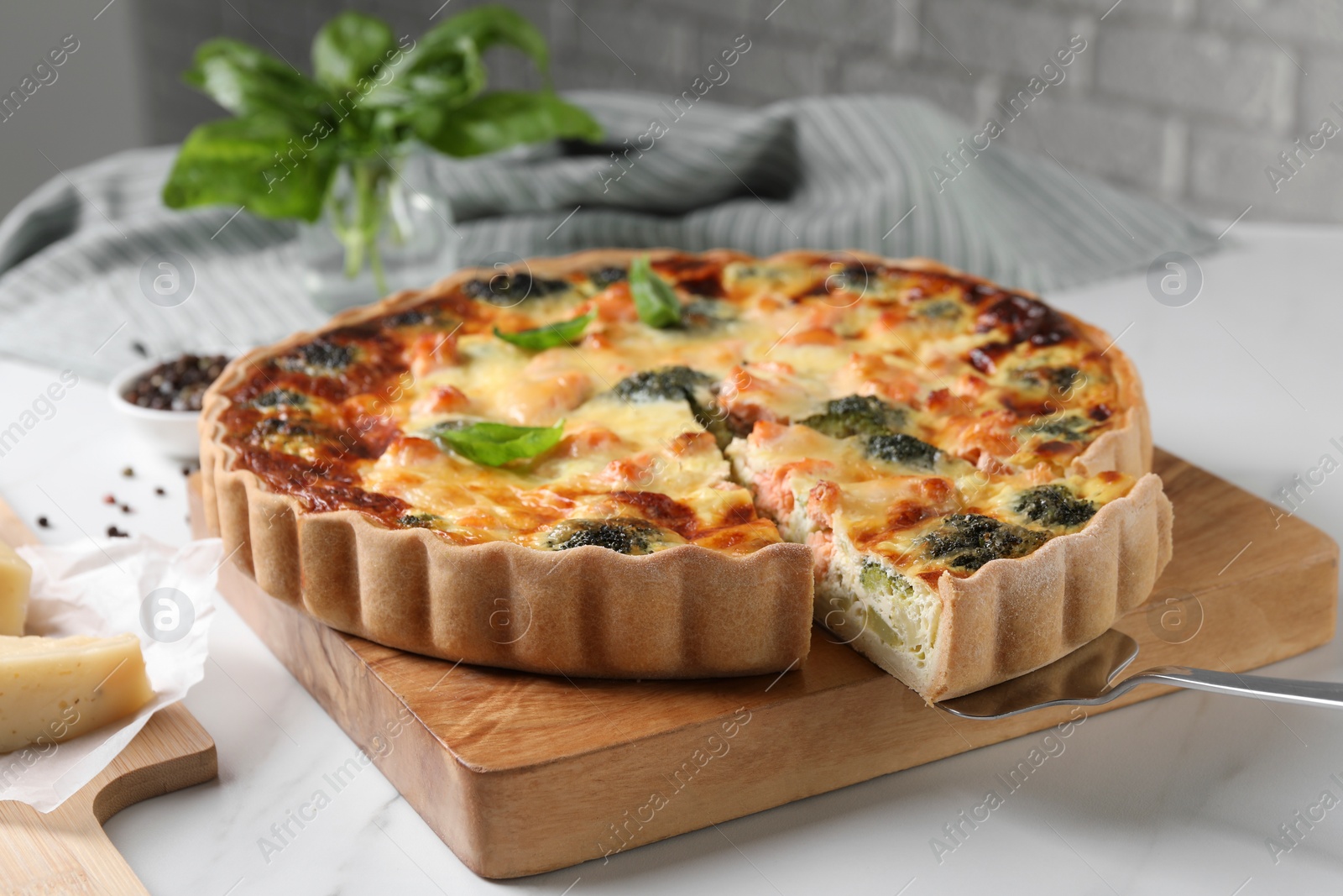 Photo of Taking piece of delicious homemade quiche with salmon and broccoli from wooden board on white table