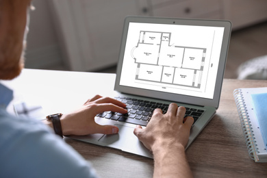 Architect making project of house on laptop at table indoors, closeup