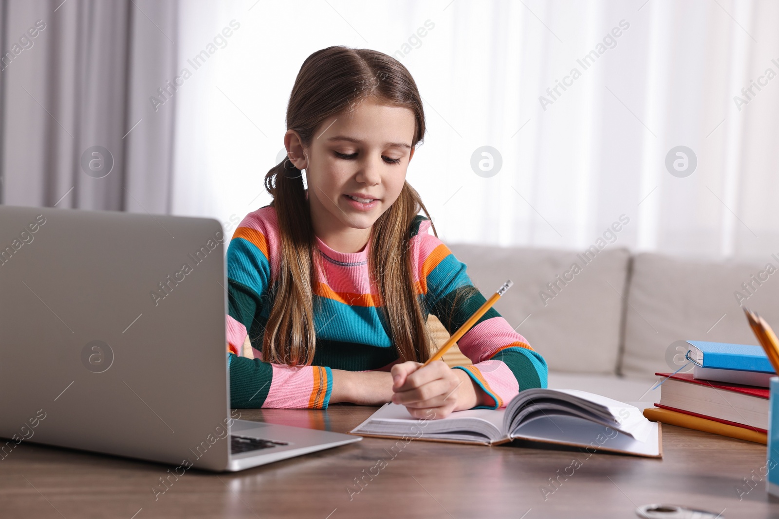 Photo of E-learning. Cute girl taking notes during online lesson at table indoors