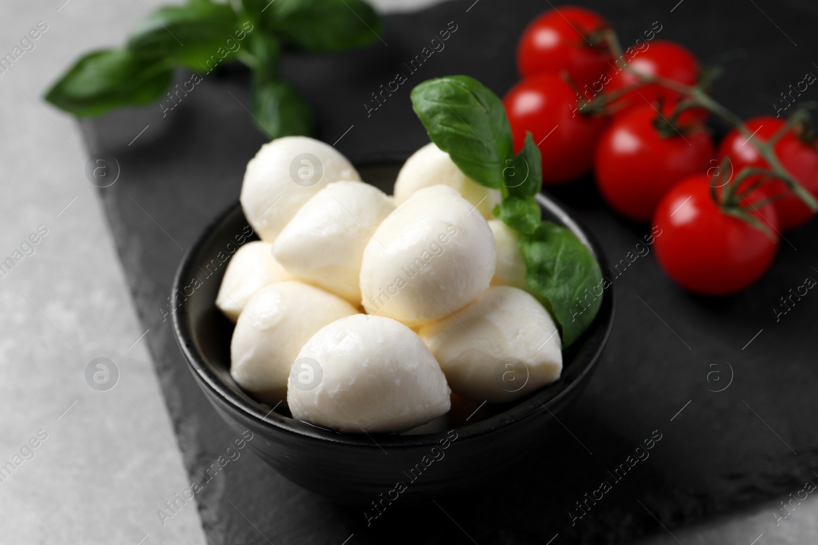 Photo of Delicious mozzarella balls, basil and tomatoes on light gray table, closeup