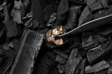 Tweezers with gold nugget above coals, closeup