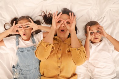 Photo of Happy mother and her children making glasses with their hands on bed, top view