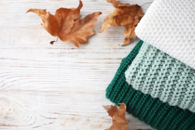 Photo of Stack of soft knitted sweaters on white wooden table. Space for text