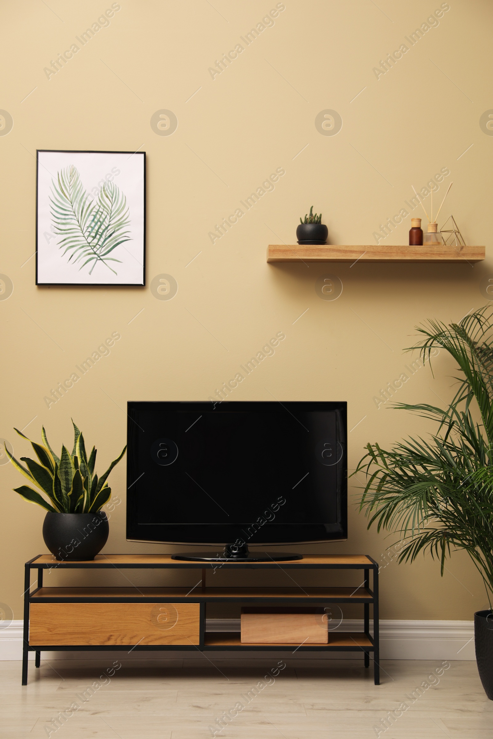 Photo of Modern TV on cabinet and green plants near beige wall in room. Interior design