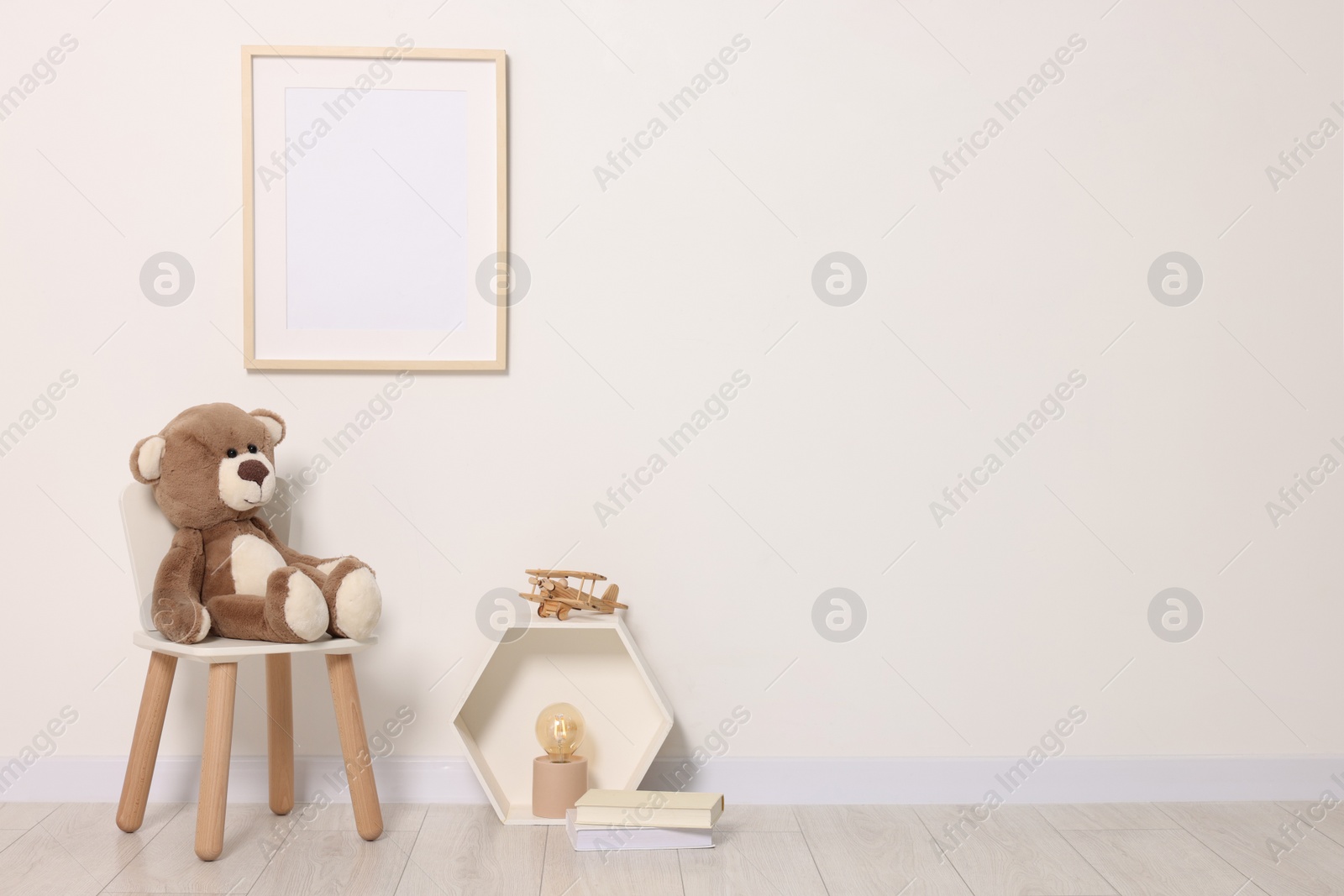 Photo of Beautiful children's room with light wall, furniture and toys, space for text. Interior design