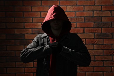 Thief in hoodie against red brick wall