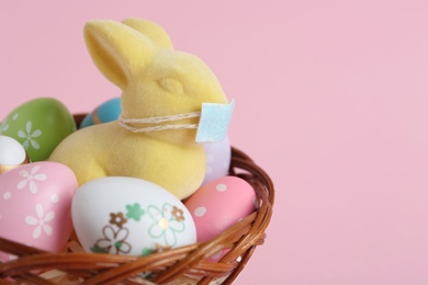 Cute bunny figure with protective mask and eggs in wicker basket on pink background, space for text. Easter holiday during COVID-19 quarantine
