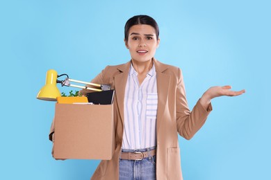 Photo of Unemployed woman with box of personal office belongings on light blue background