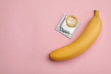 Photo of Condom with banana and space for text on pink background, flat lay. Safe sex