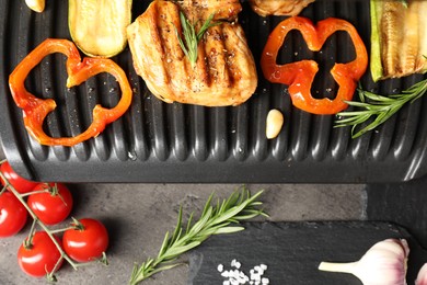 Photo of Electric grill with tasty meat, spices and vegetables on grey table, flat lay