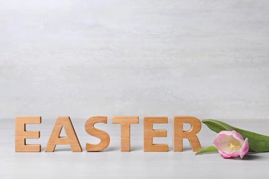 Photo of Word EASTER made of wooden letters and spring tulip on table against light background