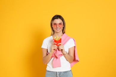 Young woman with French fries on yellow background