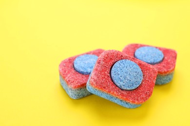 Photo of Dishwasher detergent tablets on yellow background, closeup. Space for text