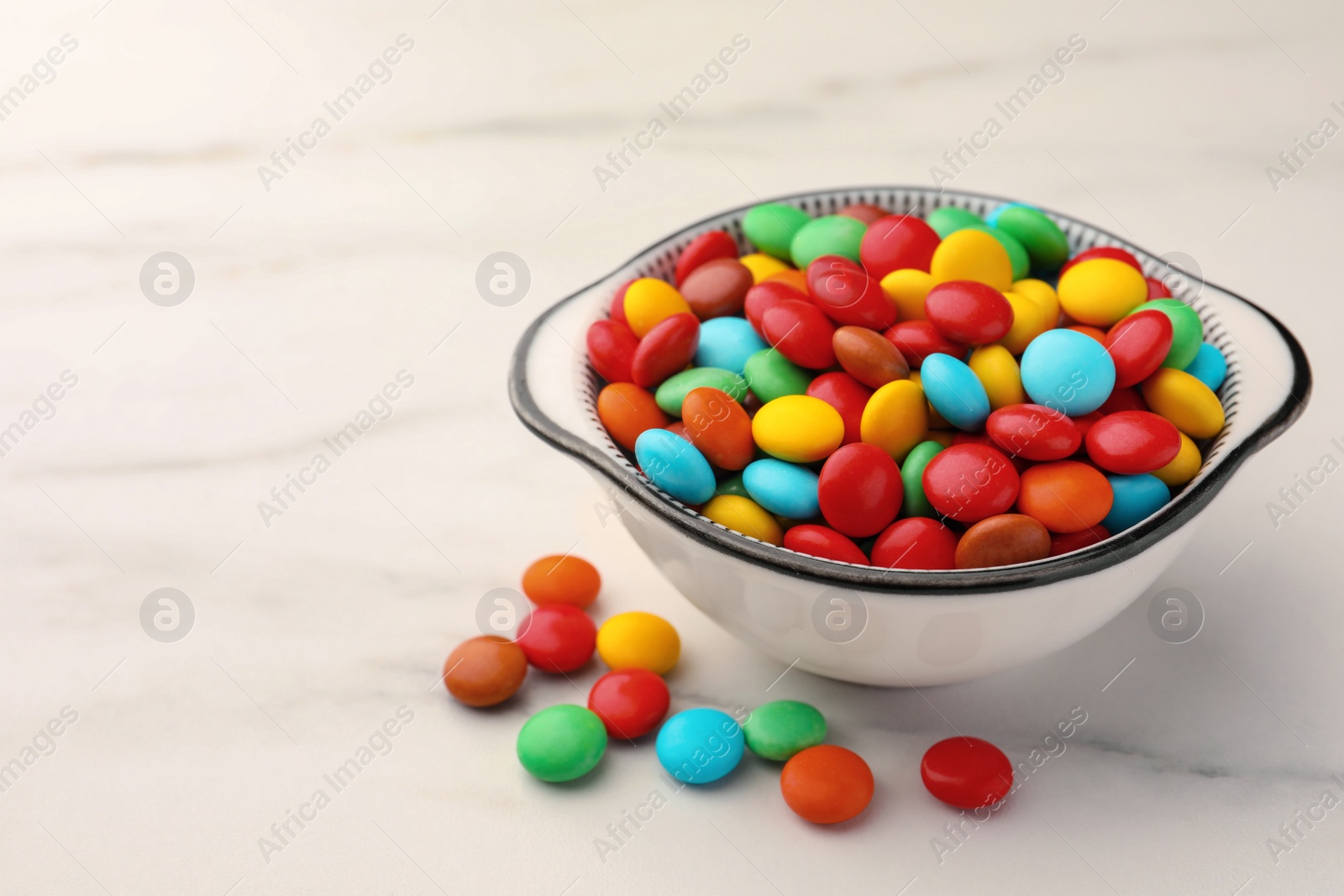 Photo of Bowl with tasty colorful candies on white marble table, space for text