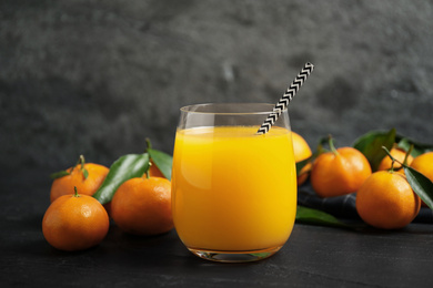 Photo of Glass of fresh tangerine juice and fruits on black table