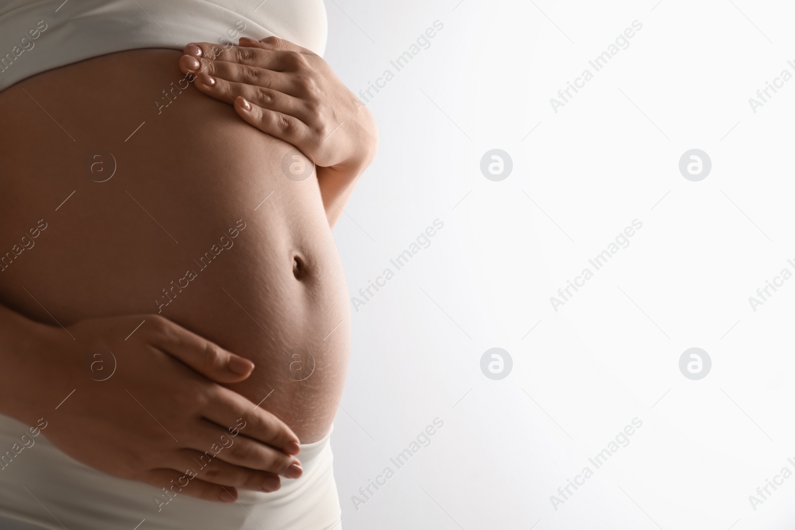 Photo of Pregnant young woman touching belly on light background, closeup. Space for text