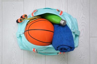 Photo of Bag with different sports equipment on wooden floor, top view