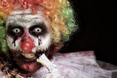 Photo of Portraitterrifying clown on black background, closeup. Halloween party costume