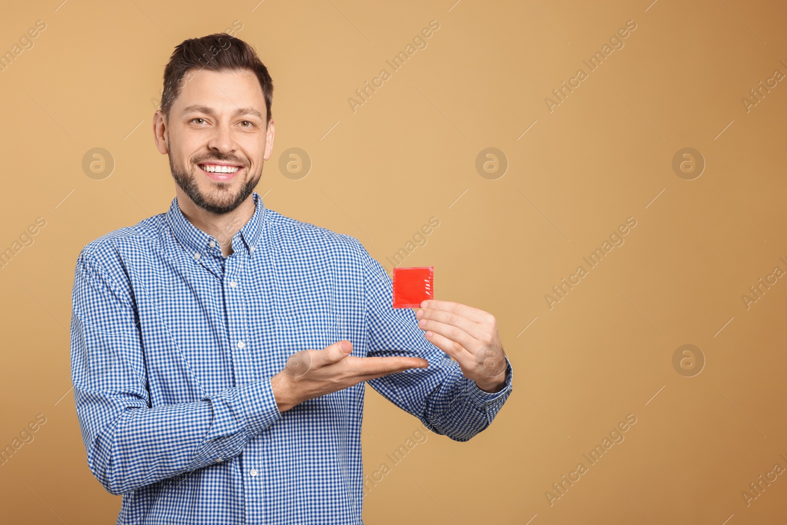 Photo of Happy man holding condom on beige background. Space for text