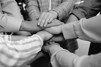 Image of People holding hands together in office, closeup. Black and white effect