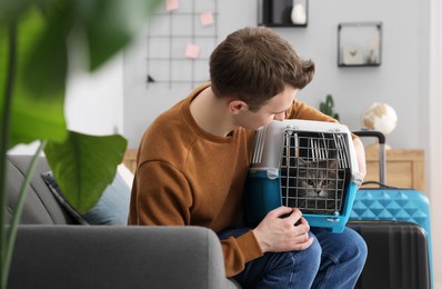 Photo of Travel with pet. Man holding carrier with cute cat on sofa at home