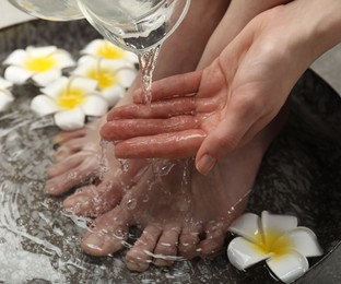 Woman pouring water onto hand while soaking her feet in bowl, closeup. Spa treatment