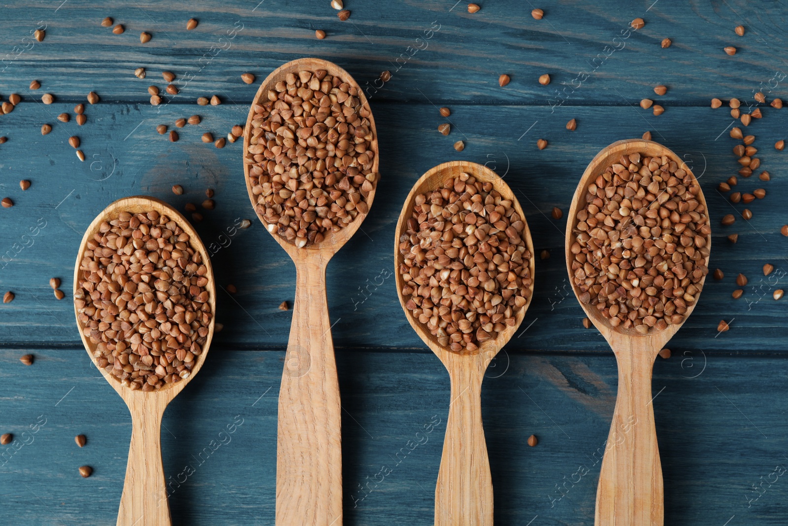 Photo of Spoons with uncooked buckwheat on wooden table, flat lay