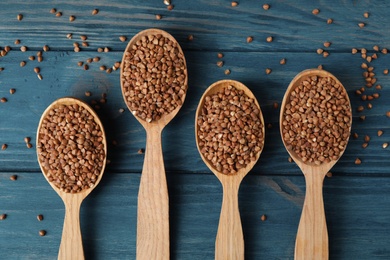 Spoons with uncooked buckwheat on wooden table, flat lay