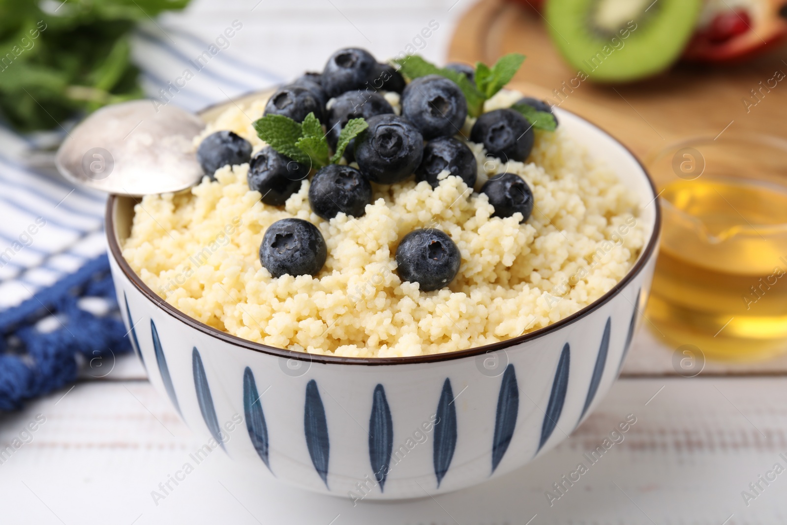 Photo of Bowl of tasty couscous with blueberries and mint on white table, closeup