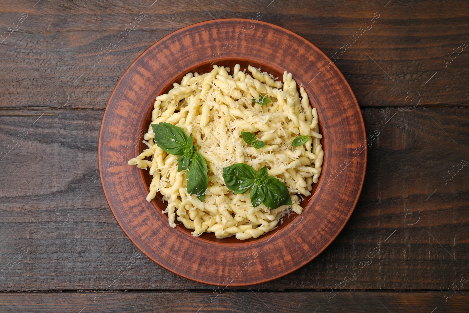 Photo of Plate of delicious trofie pasta with cheese and basil leaves on wooden table, top view