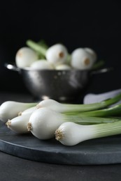 Whole green spring onions on black table, closeup