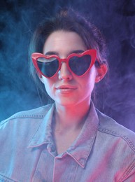 Photo of Young woman wearing sunglasses in smoke on color background