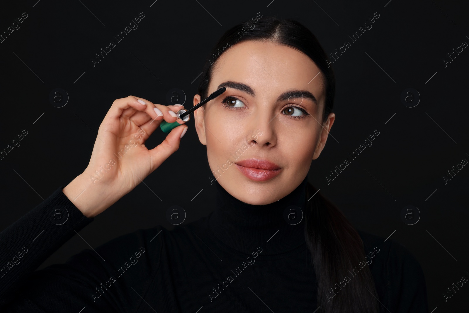 Photo of Beautiful young woman applying mascara on black background