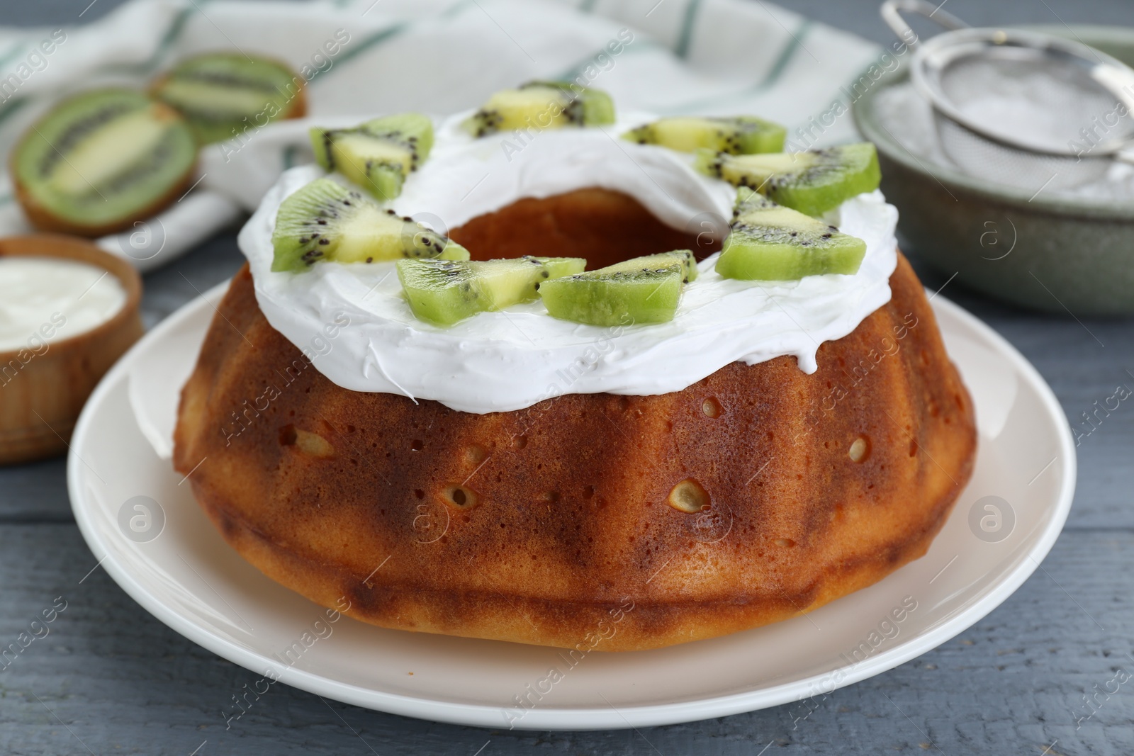 Photo of Homemade yogurt cake with kiwi and cream on grey wooden table, closeup