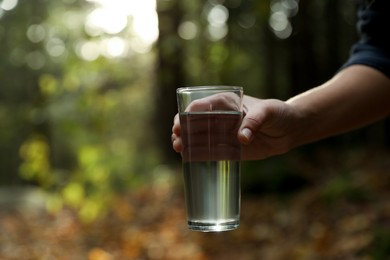 Photo of Woman holding glass of fresh water in forest, closeup. Space for text