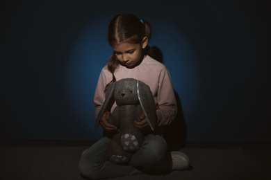 Photo of Sad little girl with toy near blue wall. Domestic violence concept