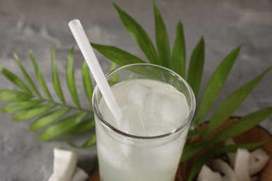 Photo of Glass of coconut water, ice cubes, leaves and nuts on grey table