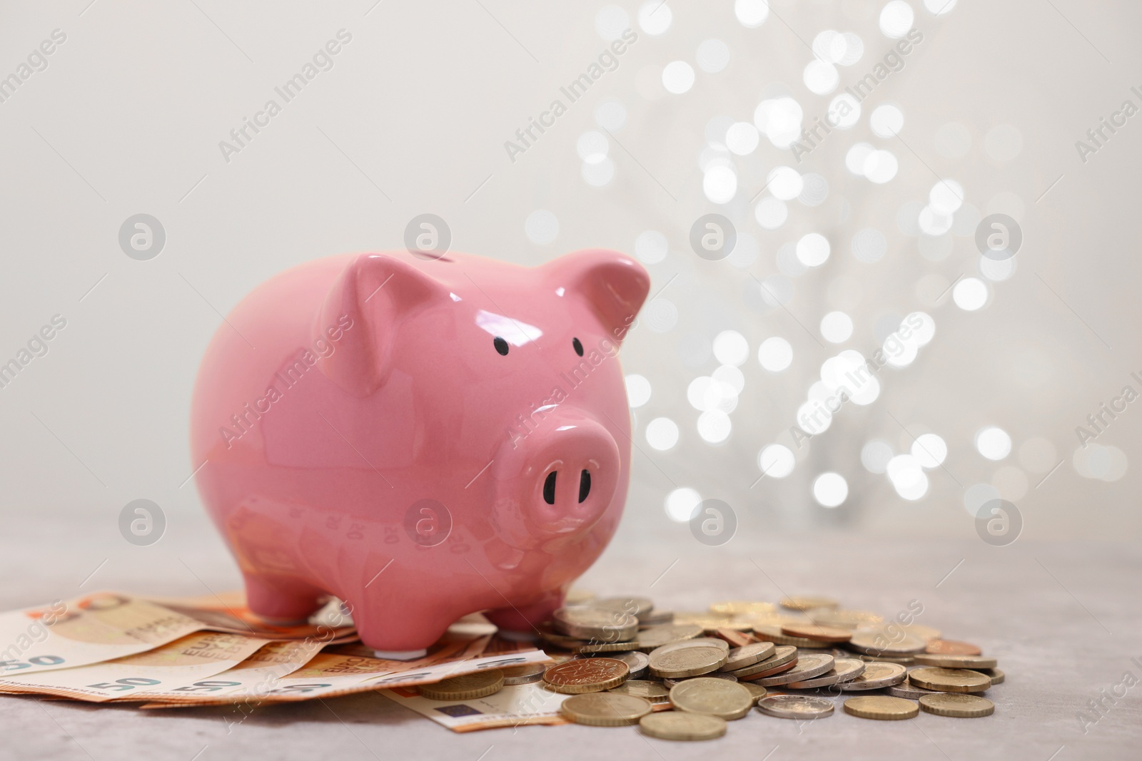 Photo of Piggy bank with euro banknotes and coins on grey table against blurred lights, space for text