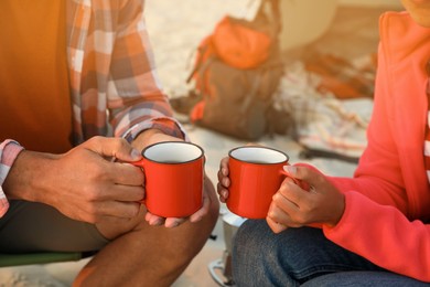 Photo of Couple with cups of hot drinks outdoors, closeup. Beach camping