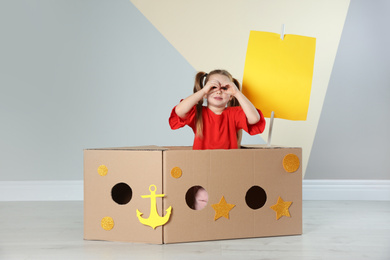 Photo of Cute little child playing with cardboard ship near color wall