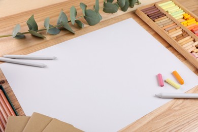 Photo of Blank paper, soft pastels and drawing pencils on wooden table at artist's workplace. Space for design