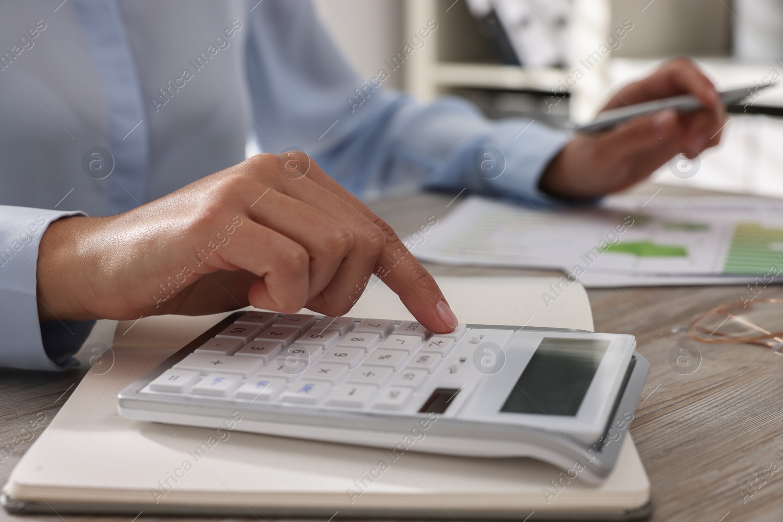 Photo of Woman using calculator at light wooden table in office, closeup