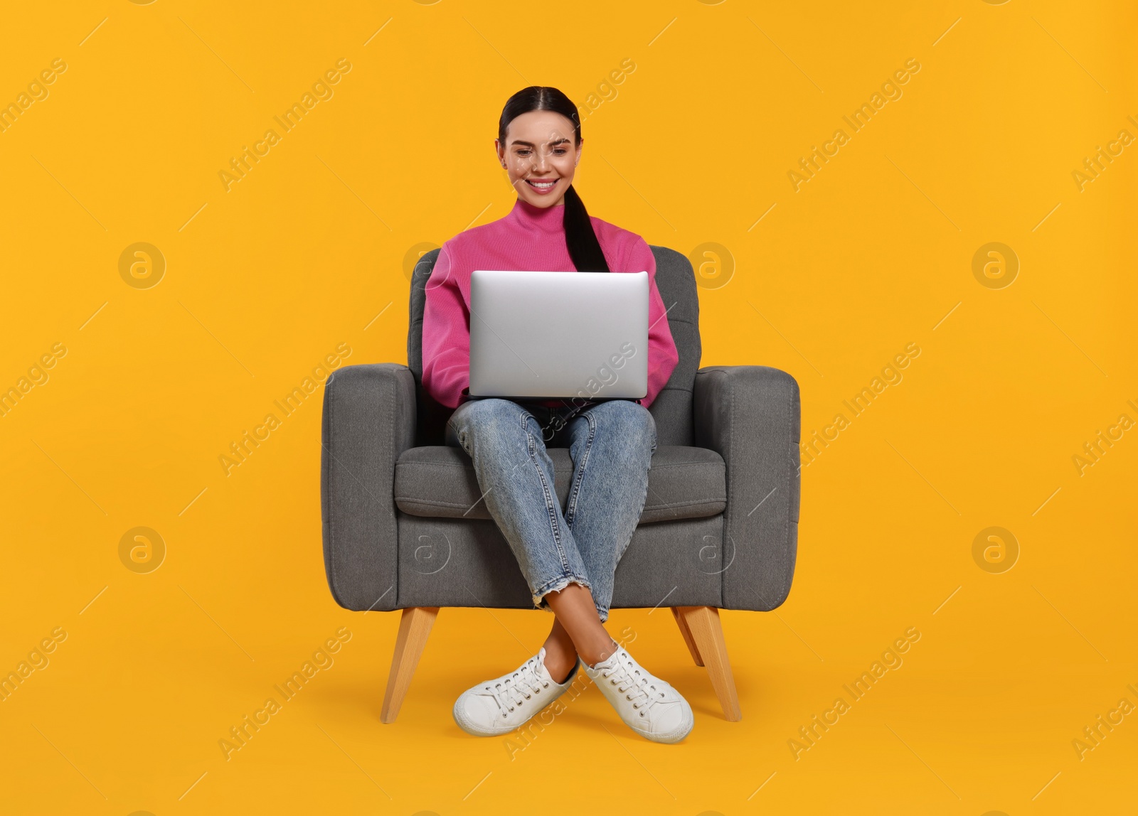 Photo of Happy woman with laptop sitting in armchair on orange background