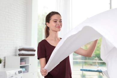 Photo of Young woman with clean bedsheet indoors. Laundry day