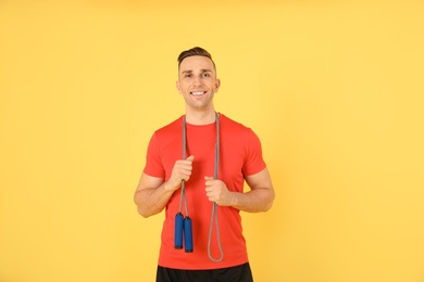 Portrait of young sportive man with jump rope on color background