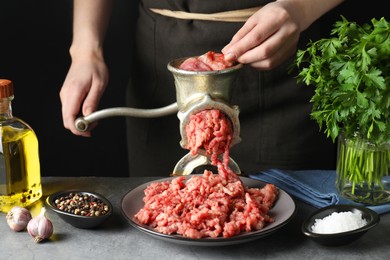 Photo of Woman making beef mince with manual meat grinder at grey table, closeup