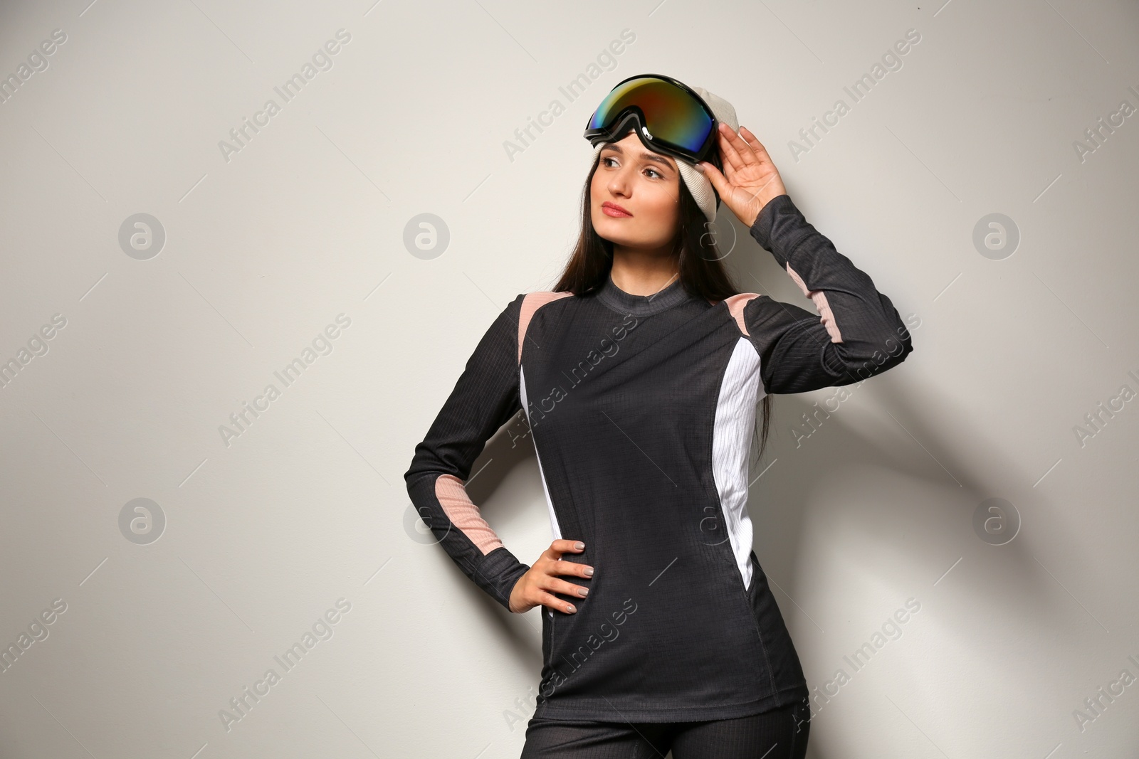 Photo of Woman wearing thermal underwear and goggles on light grey background. Winter sport clothes